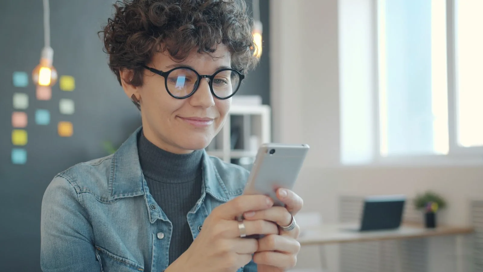 Une collaboratrice sourit en lisant un message sur son téléphone, dans un bureau lumineux